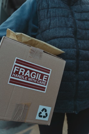 Osoba trzymająca karton z napisem "fragile. Handle with care". 