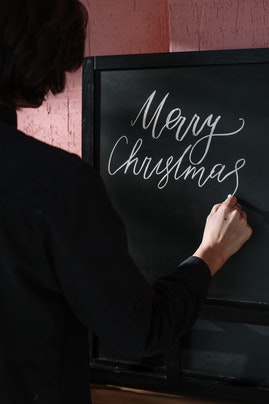 Osoba pisząca Merry Christmas na czarnej tablicy.