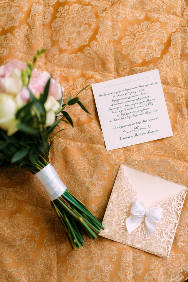 Na haftowanym tle leży bukiet kwiatów oraz zaproszenie ślubne.