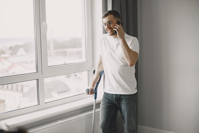 Osoba o kulach rozmawiająca przez telefon przy oknie
