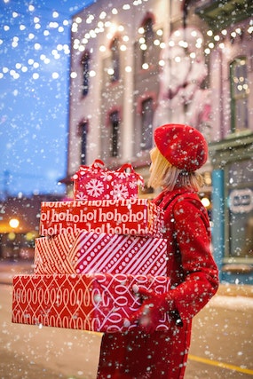 Kobieta trzymająca stos świątecznych prezentów. Dookoła pada śnieg.