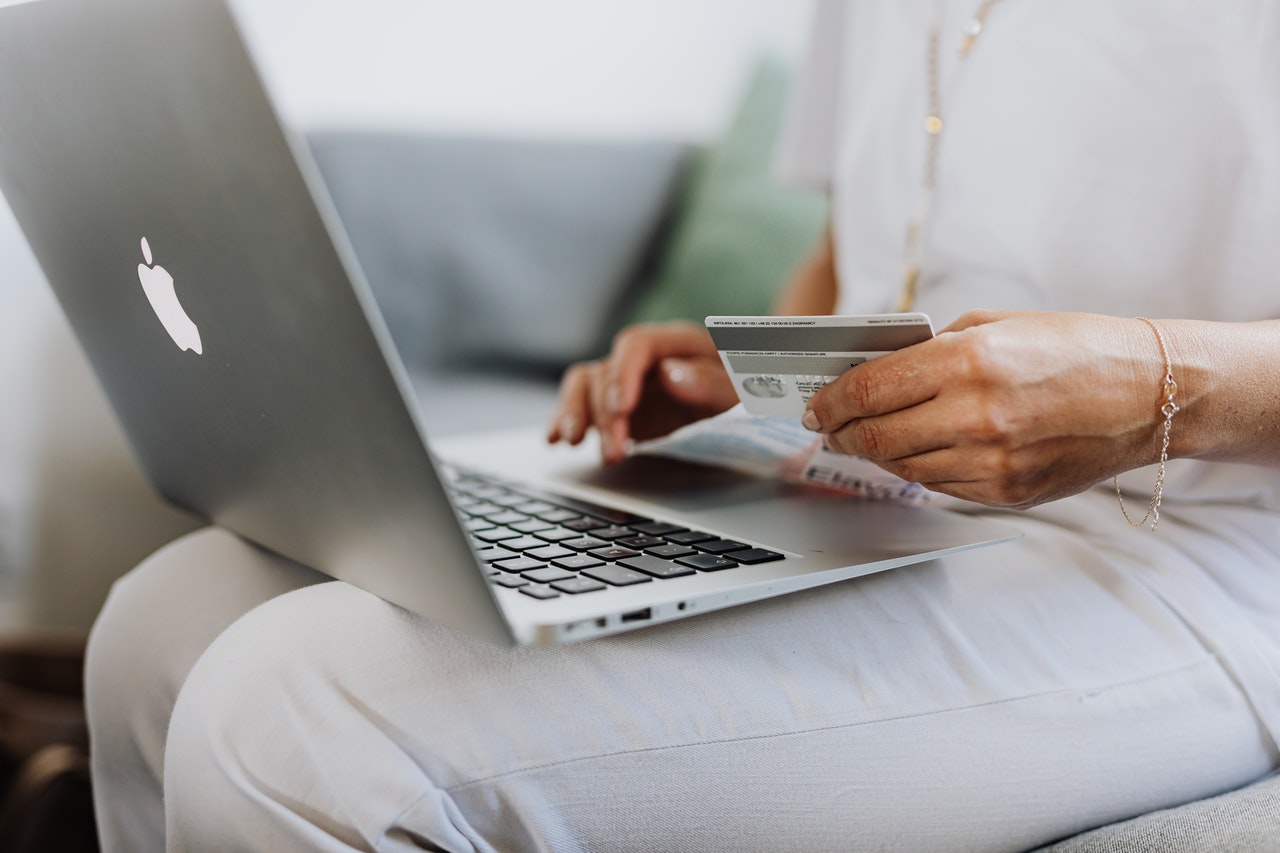 Osoba używająca laptopa, w drugiej ręce trzyma kartę kredytową.