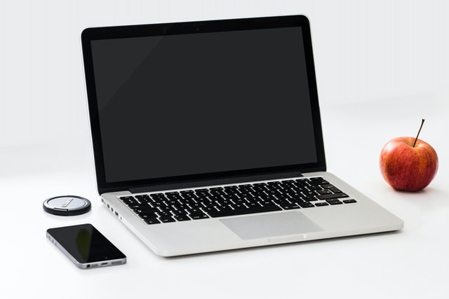 Na środku jest laptop, obok leży smartfon oraz jabłko.