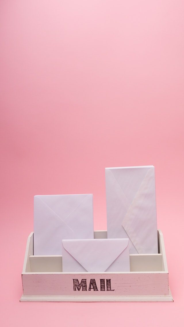 Na różowym tle jest biała skrzyneczka z napisem mail, w której są trzy koperty.