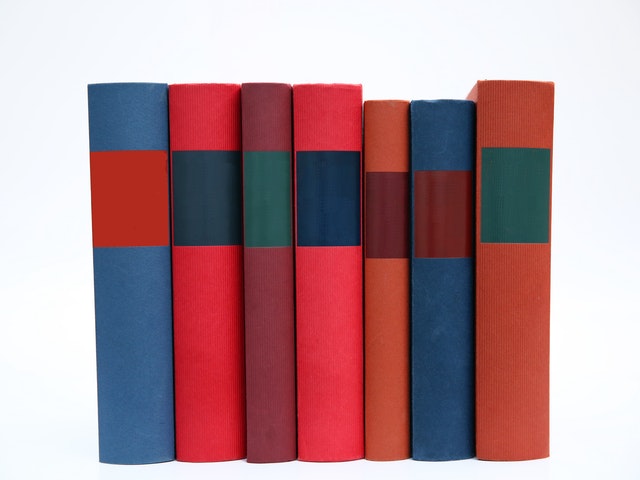 7 książek ustawionych grzbietami o różnych kolorach i wielkościach.