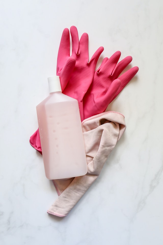 Różowe gumowe rękawice, pudrowa ściereczka i butelka.