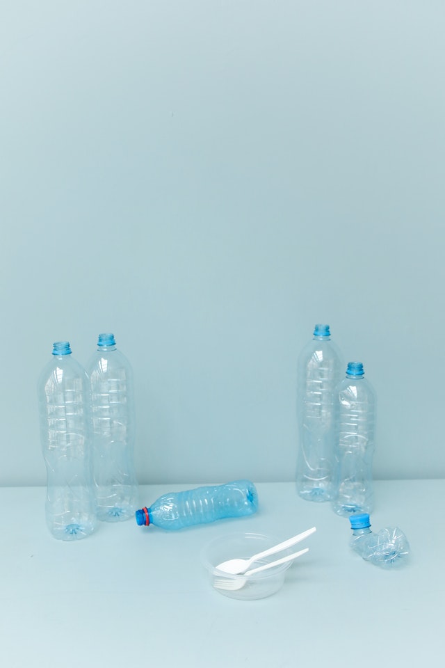 Cztery stojące butelki plastikowe, jedna leżąca, jedna zgnieciona, plastikowy talerzyk i sztućce.