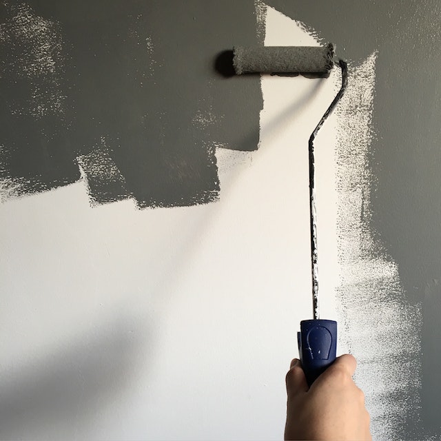 Dłoń malująca wałkiem białą ścianę na szaro.