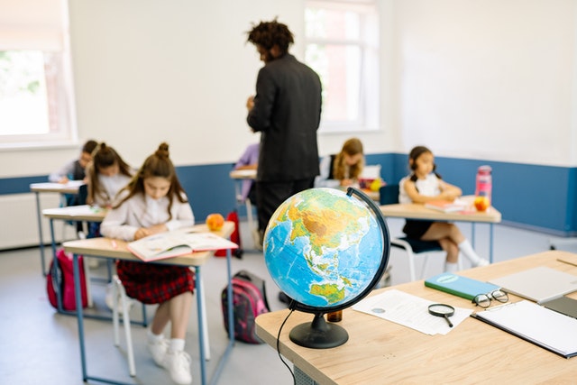 Globus na tle jasnej klasy z uczniami i nauczycielem.